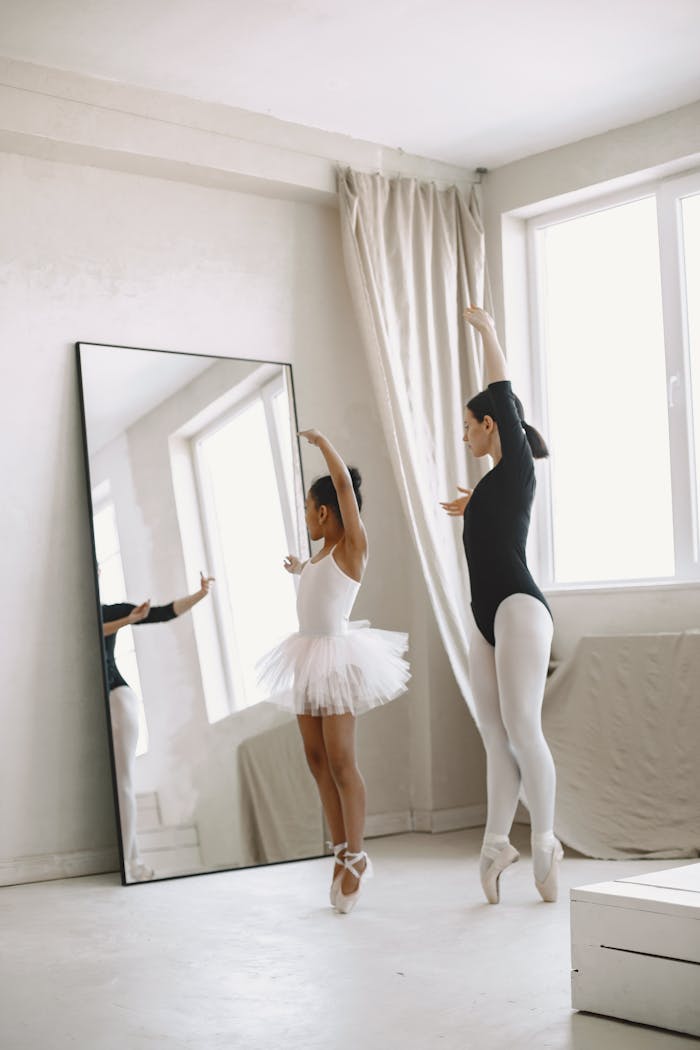 Home A young girl practices ballet with a teacher in a bright dance studio.